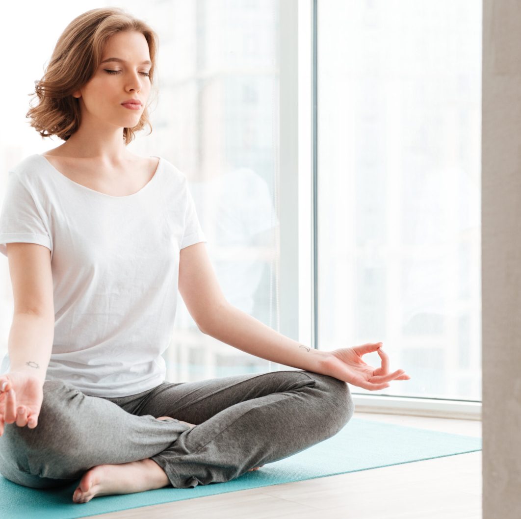 Image of young beautiful lady sitting near window make yoga exercises.